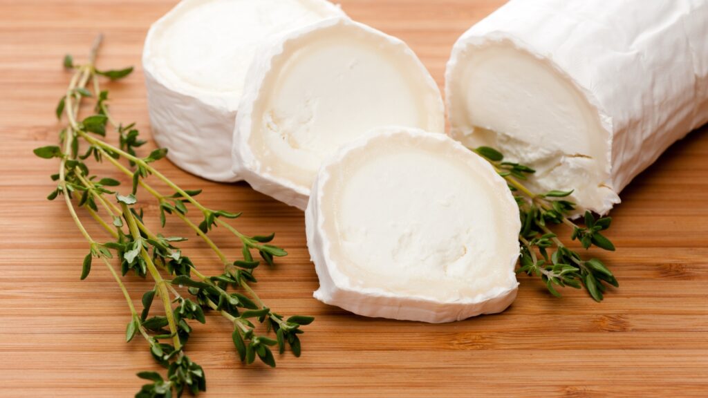 A piece of herb-infused cheese on a wooden cutting board.