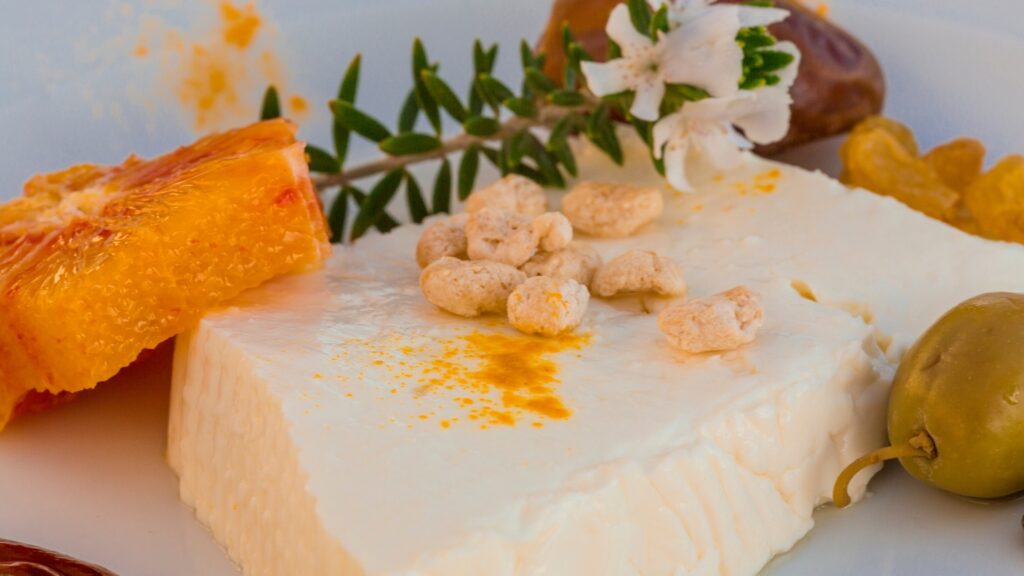 A piece of cheese infused  on herb a wooden cutting board.